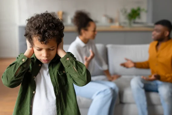 A child covers his ears while his parents argue in the background