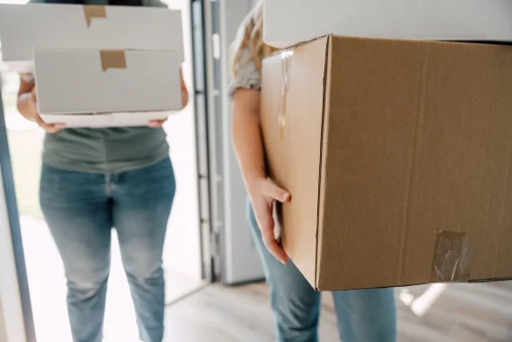 A couple carrying cardboard boxes into a house