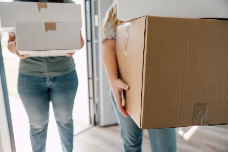 A couple carrying cardboard boxes into a house